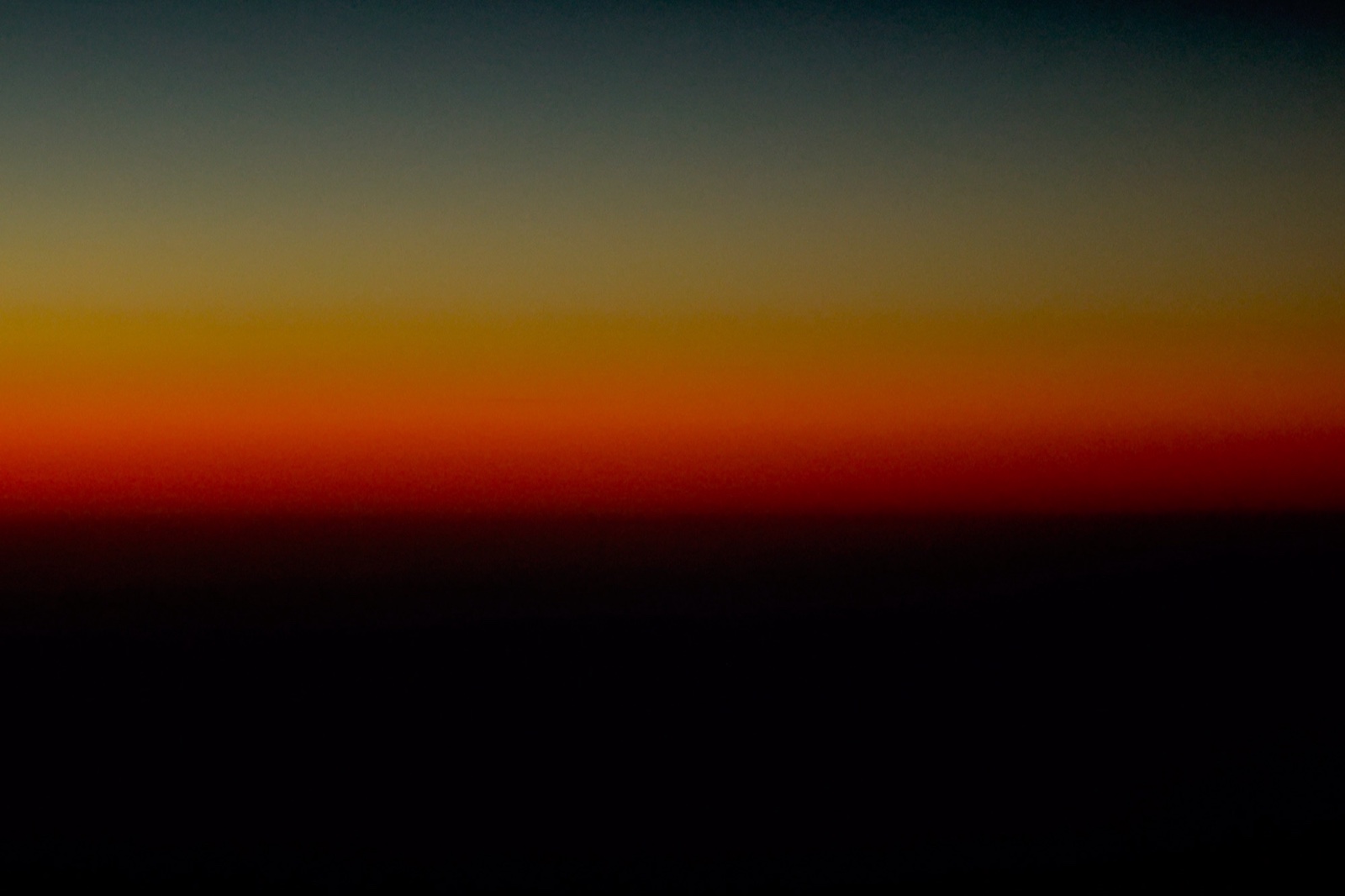 Bandas horizontales de color puro al anochecer visto desde el aire; de arriba abajo, un verde grisáceo se funde en amarillo, naranja y rojo intenso antes de disolverse en negro.