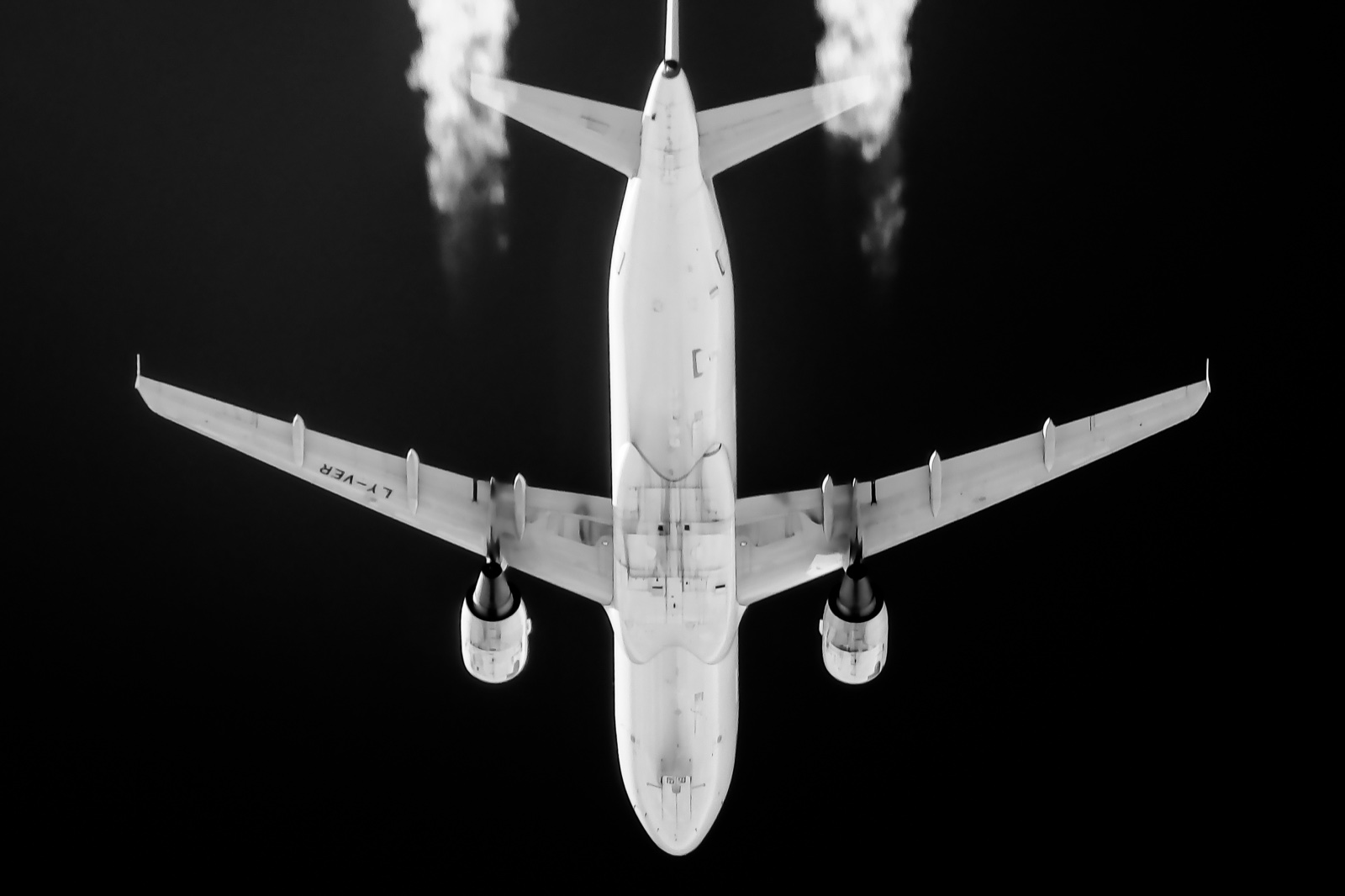 Avión de pasajeros visto desde abajo contra un cielo negro, con dos estelas de condensación que nacen en los motores.