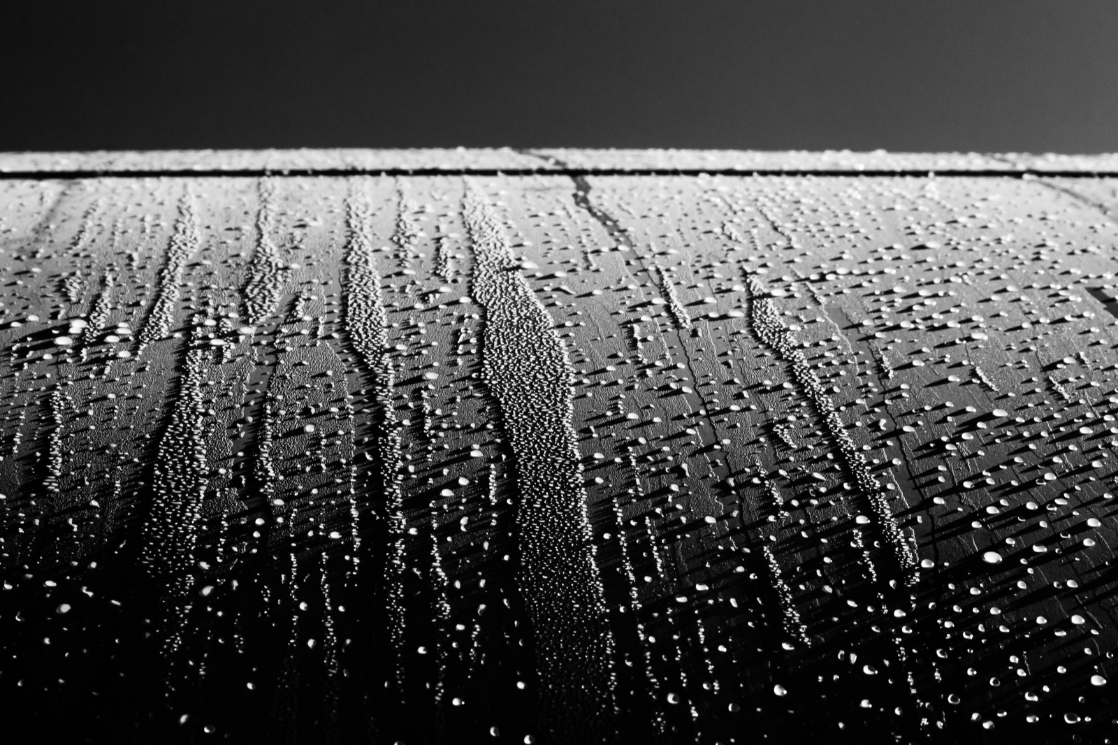 Gotas de rocío y regueros de agua sobre la superficie curva y oscura de un fuselaje, con el cielo gris al fondo.