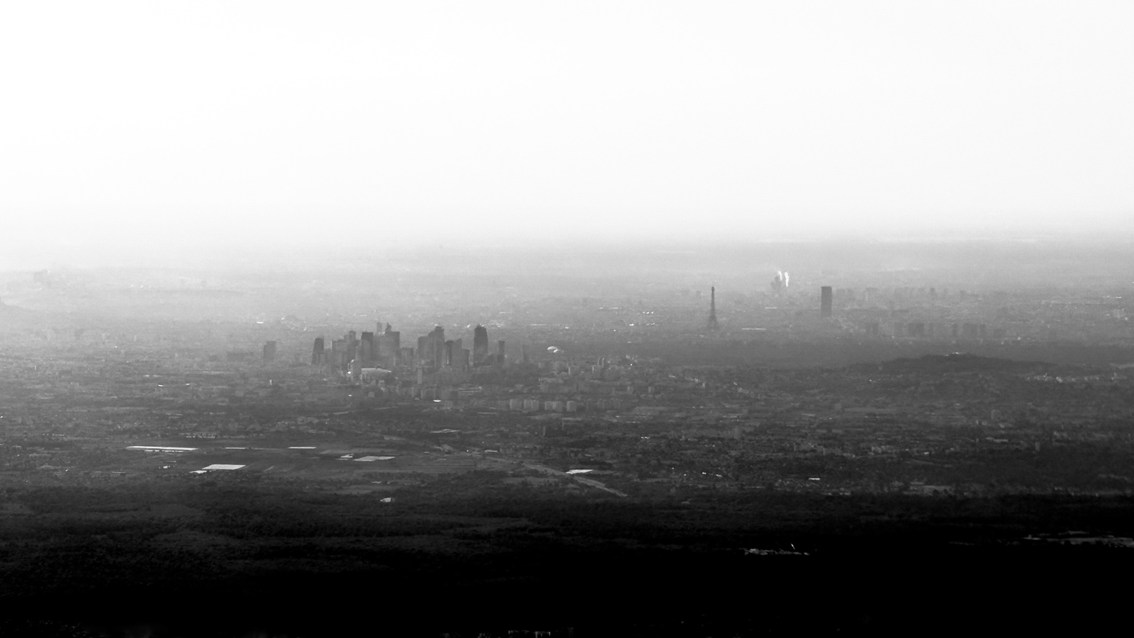 Vista aérea de una gran ciudad entre la calima, con un grupo de rascacielos y la torre Eiffel recortados sobre el gris.