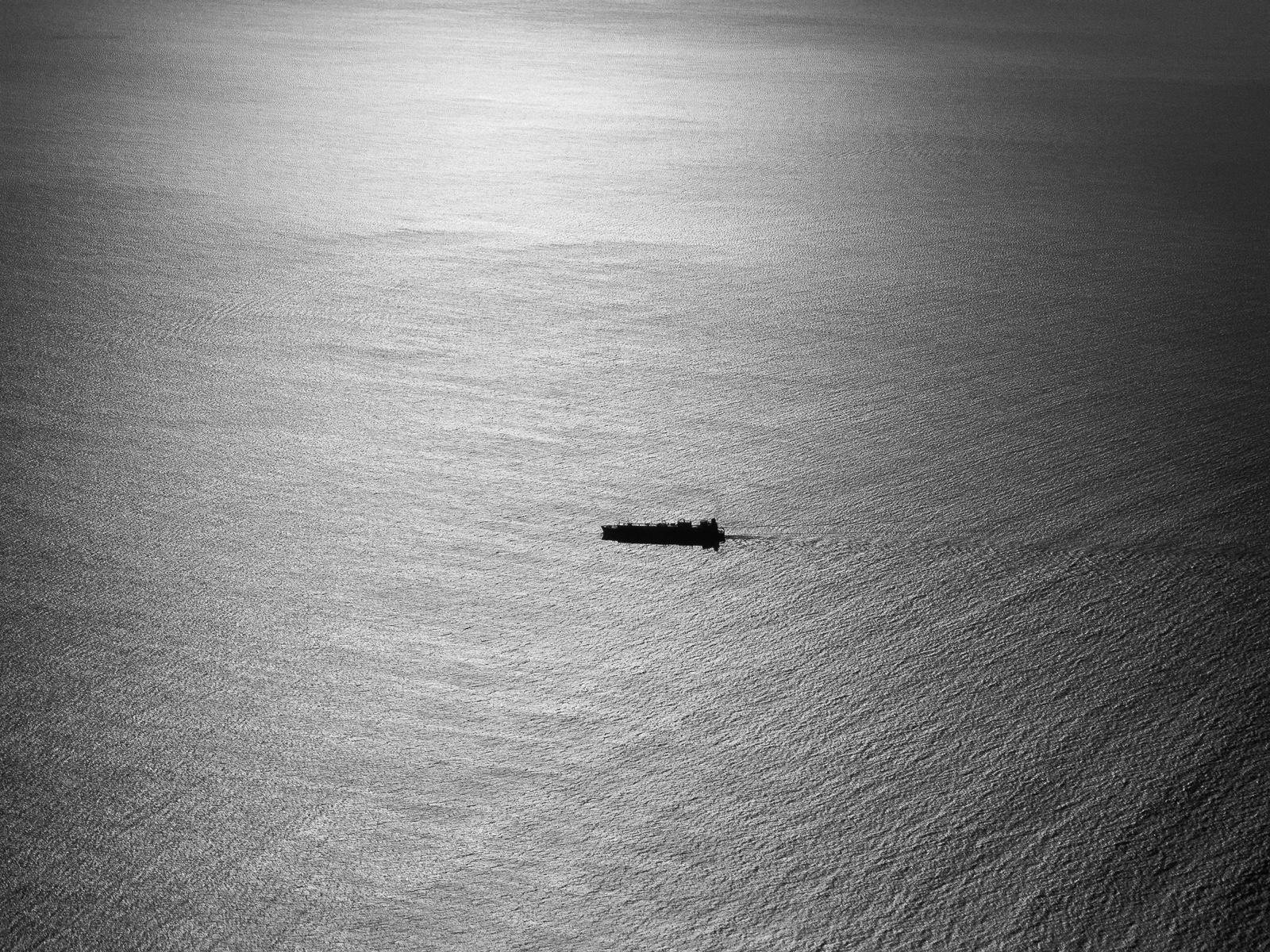 Un carguero solo en medio de un mar plateado por el sol, visto desde muy alto.